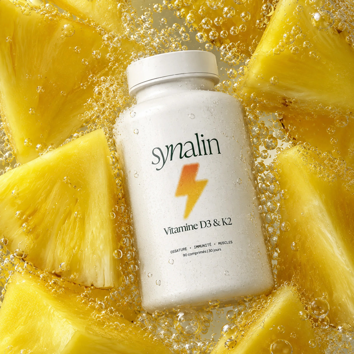 Pilulier Synalin Vitamine D3 & K2 posé sur des morceaux d’ananas