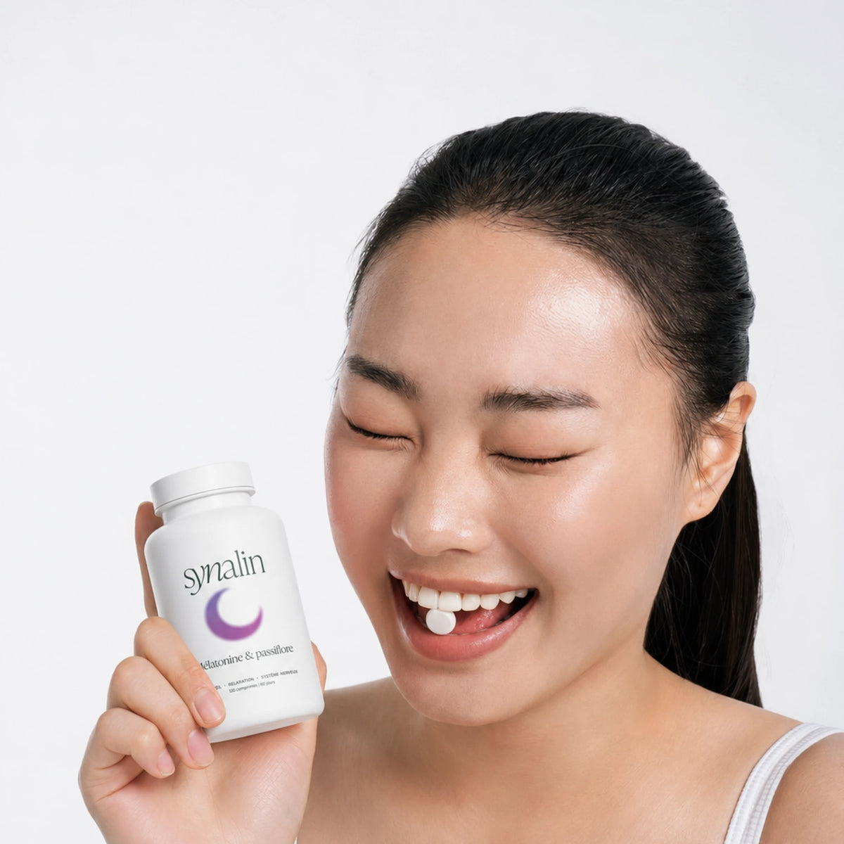 Femme souriante tenant le pilulier Synalin Mélatonine & Passiflore et un comprimé