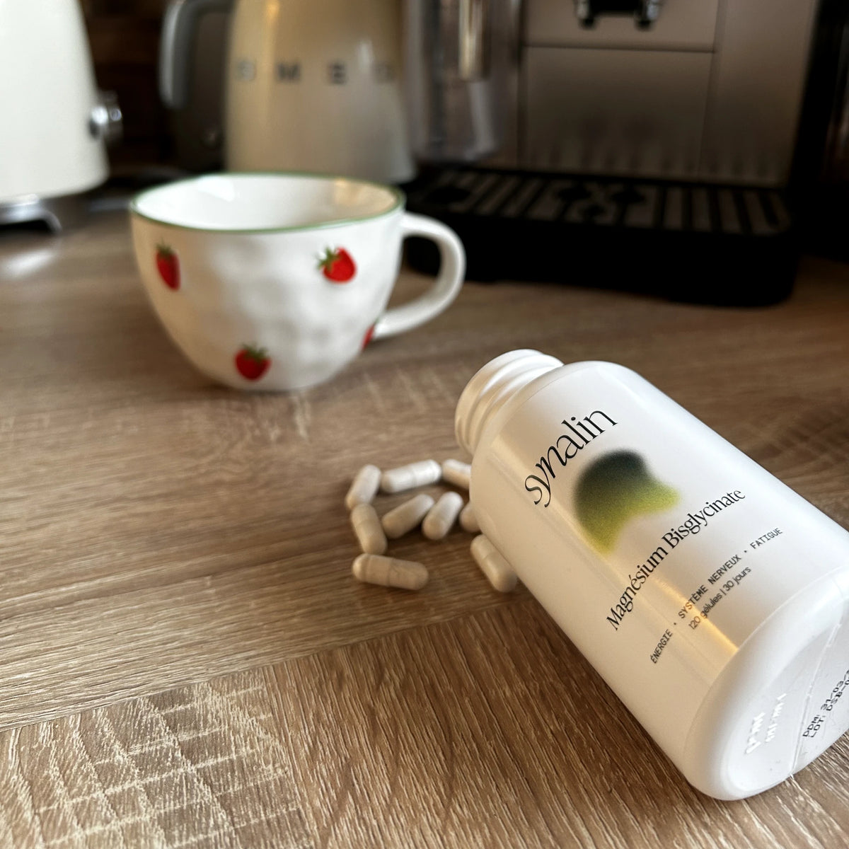 Pilulier Synalin Magnésium Bisglycinate et gélules sur un plan de travail de cuisine, à côté d’une tasse